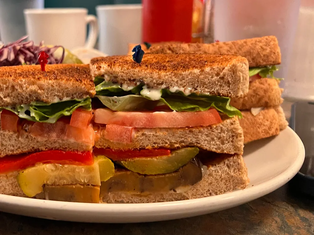 Triple-decker club sandwich on toasted brown bread with lettuce and tomato
